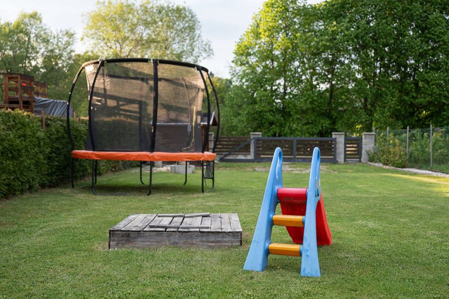 Trampolína se sítí, pískoviště a barevná skluzavka na trávníku